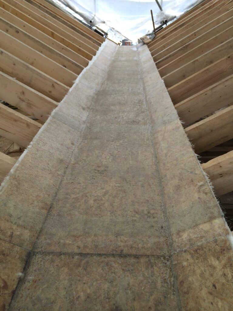 Internal view looking up along a wide lead valley lining sitting between timber roof rafters, with a temporary scaffold sheeting canopy overhead and tools visible at the ridge level